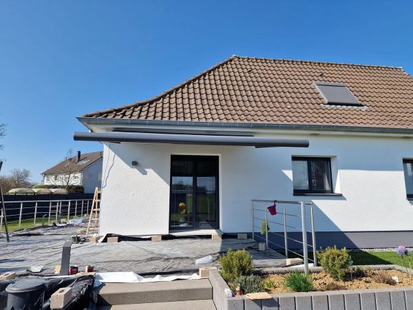 Geschlossene anthrazit Kassettenmarkise unter der Traufe eines weißen Ziegeldachhauses