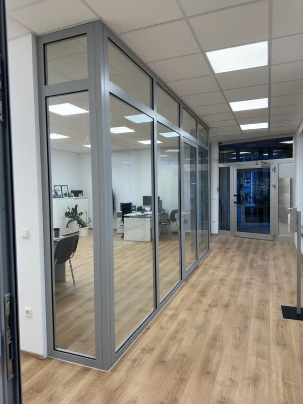 Glastrennwand aus grauem Aluminium mit Tür zwischen Büro und Flur mit hellem Boden