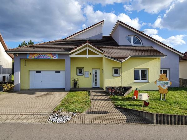 Gelb-fliederfarbenes Gebäude mit weißem Sektionaltor, weißer Haustür mit Glasstreifen und weißen Fenstern