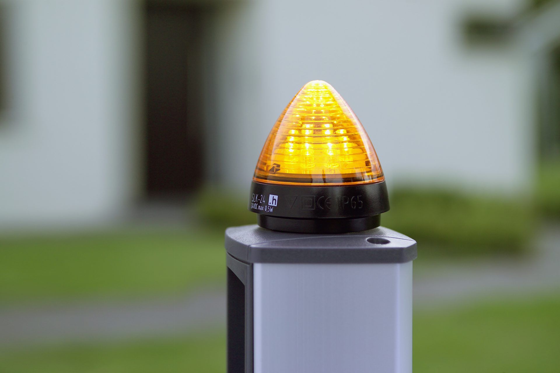 Leuchtende orange Hörmann-Signalleuchte SLK 24 auf einer Säule, die die Torbewegung anzeigt