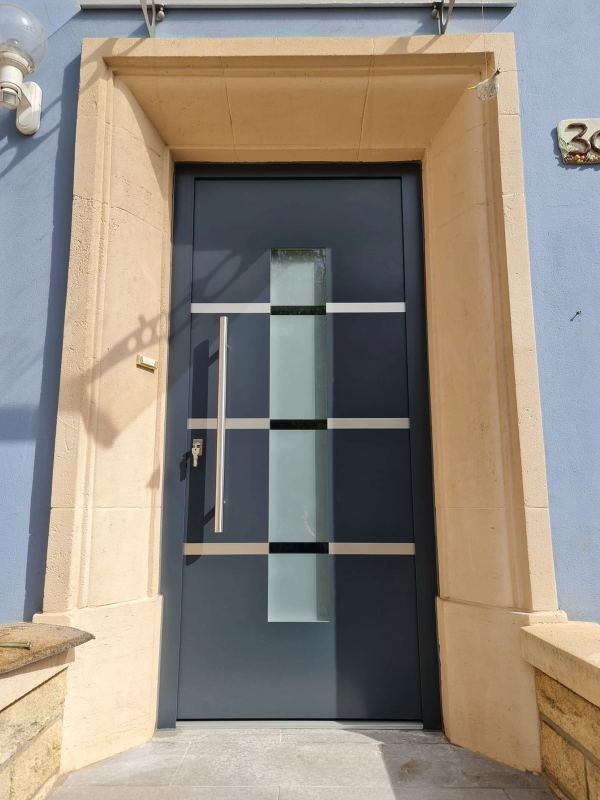 Anthrazitfarbene Haustür mit Milchglas und waagerechten Edelstahlbändern in Sandsteingewände, blaue Fassade