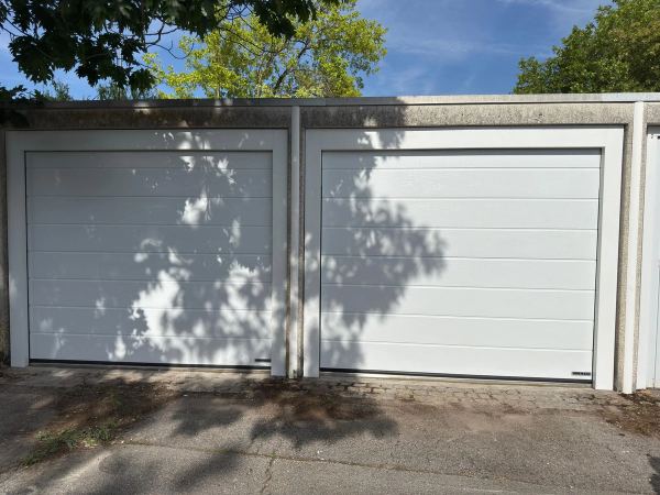 Zwei weiße Sektionaltore mit Sicken in einer Garagenreihe, Baumschatten