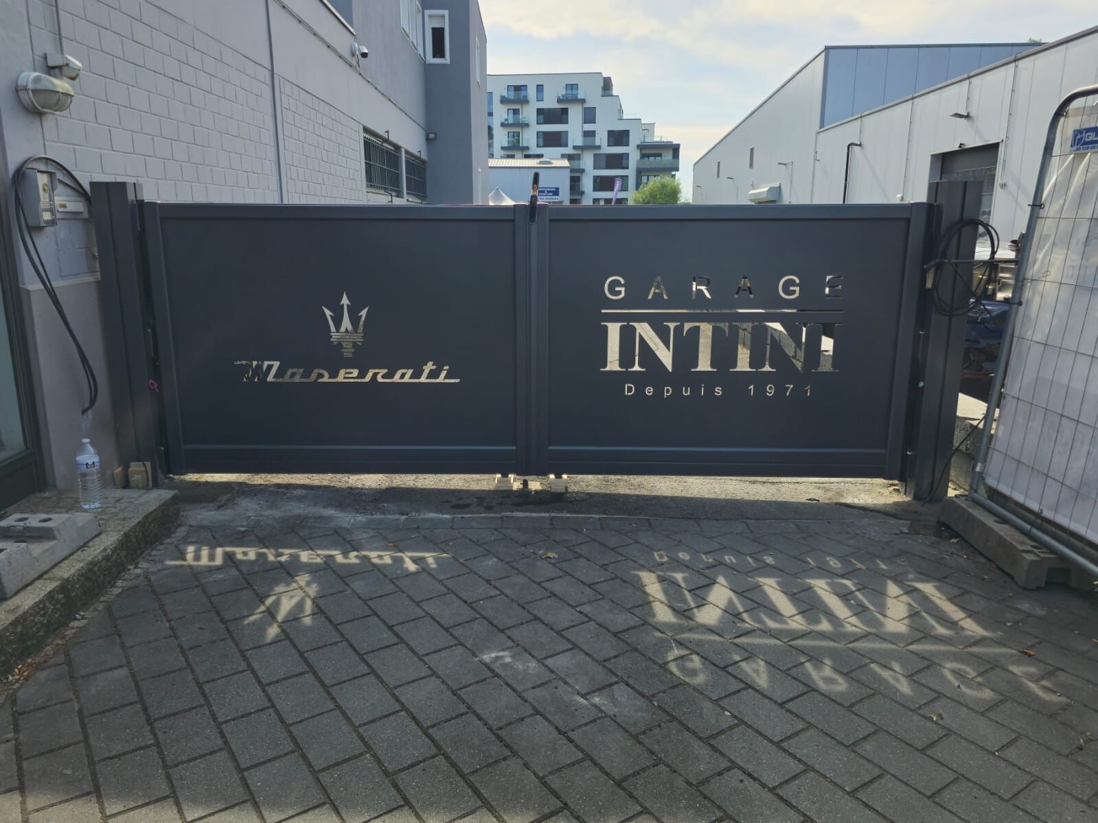 Zweiflügeliges anthrazitfarbenes Tor mit ausgeschnittenem Schriftzug und Logo einer Autowerkstatt