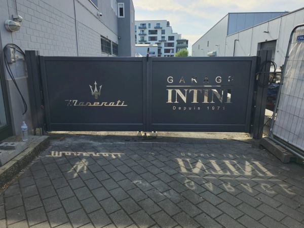 Zweiflügeliges anthrazitfarbenes Tor mit ausgeschnittenem Schriftzug und Logo einer Autowerkstatt