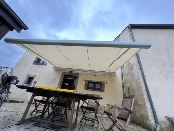 Ecrufarbene Markise ausgefahren über Terrasse eines alten Landhauses