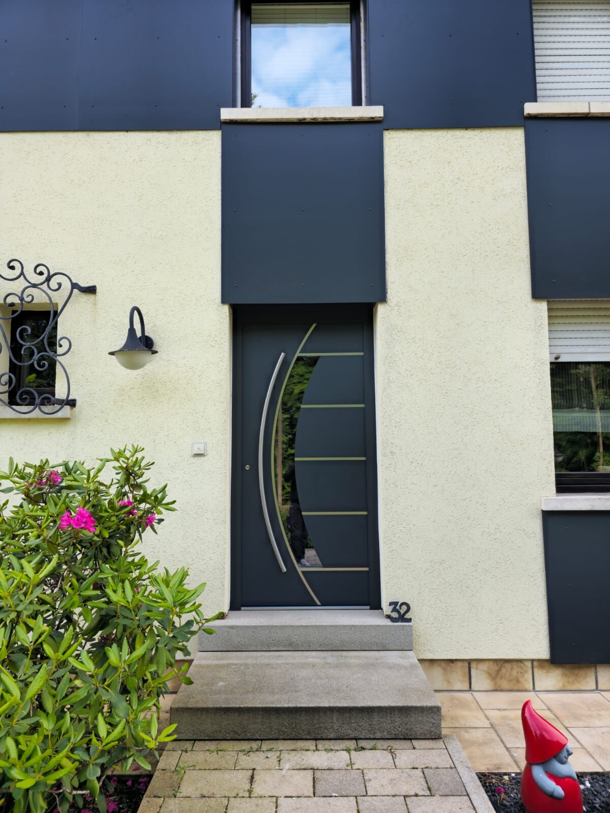 Anthrazit Haustür mit geschwungenem Glasausschnitt, Edelstahl-Lisenen und Bogengriff, cremefarbene Fassade