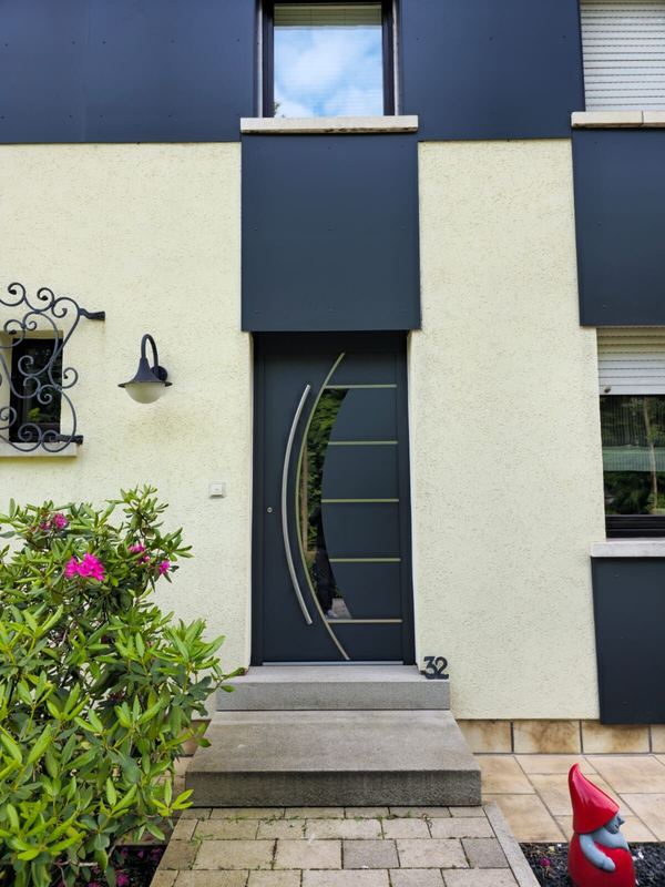 Anthrazit Haustür mit geschwungenem Glasausschnitt, Edelstahl-Lisenen und Bogengriff, cremefarbene Fassade