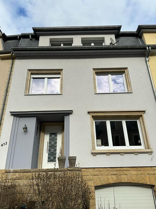 Graues Stadthaus mit weißen Fenstern in Steinlaibungen und weißer Haustür mit schmiedeeisernem Gitter