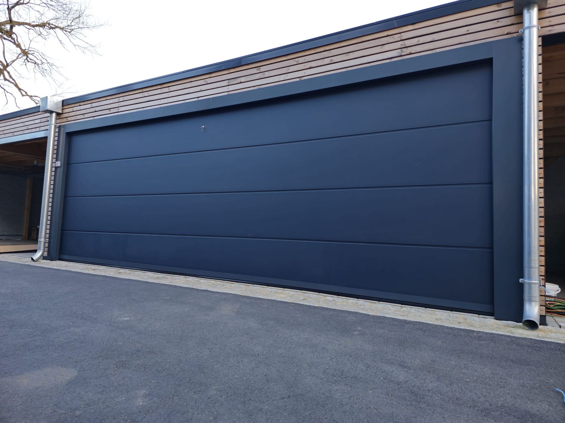 Très large porte de garage sectionnelle gris ardoise lisse sur un garage moderne bardé de bois