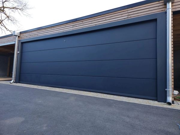 Sehr breites, glattes schiefergraues Sektionaltor an einer modernen Garage mit Holzverschalung