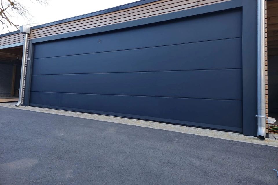 Very wide smooth slate grey sectional garage door on a modern timber-clad garage