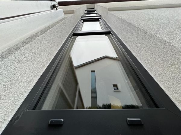 Hohes, schmales Festfenster mit anthrazitfarbenem Rahmen in weißer Putzfassade, Froschperspektive