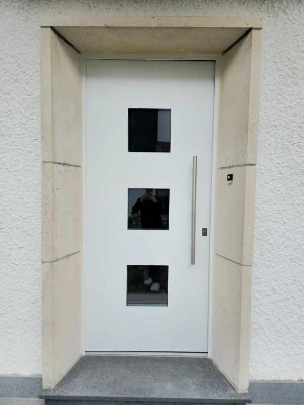 Weiße Haustür mit drei quadratischen getönten Glasfeldern und Stangengriff im Sandsteingewände