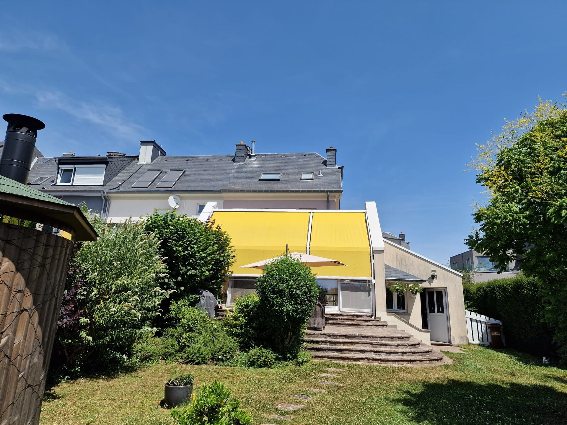 Gelbe Wintergartenmarkise auf dem Glasdach eines Anbaus mit Garten