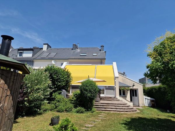 Gelbe Wintergartenmarkise auf dem Glasdach eines Anbaus mit Garten