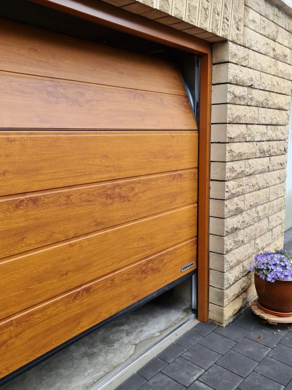 Hörmann-Sektionaltor in Golden Oak beim Öffnen, Sandsteinmauer und Blumentopf