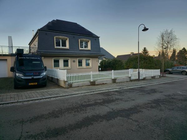 Weißer Lattenzaun auf Sockelmauer um ein Haus mit Mansarddach und Solarmodulen