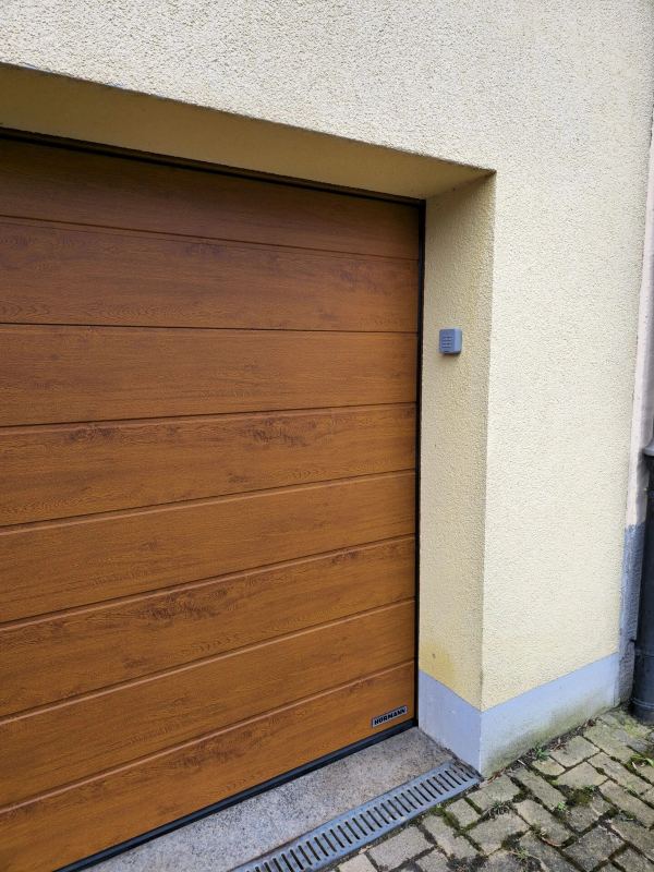 Hörmann-Sektionaltor in Golden-Oak-Dekor mit Codetaster an hellgelb verputzter Fassade