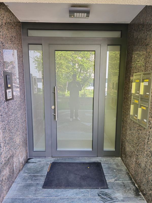 Hauseingang eines Wohnhauses: graue Aluminium-Glastür mit Seitenteilen und Oberlicht, Granitwände