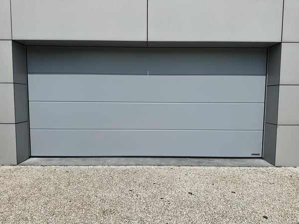 Glattes hellgraues Sektionaltor in einer Fassade aus großformatigen Platten, Kiesboden