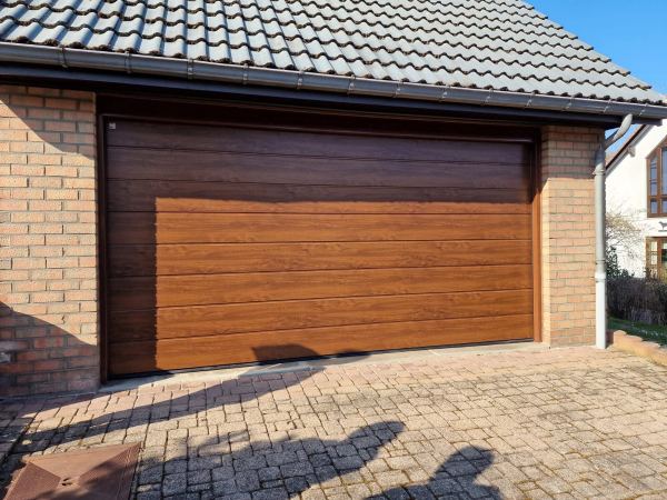 Doppel-Sektionaltor in Golden-Oak-Holzoptik zwischen Klinkermauern unter einem Ziegeldach