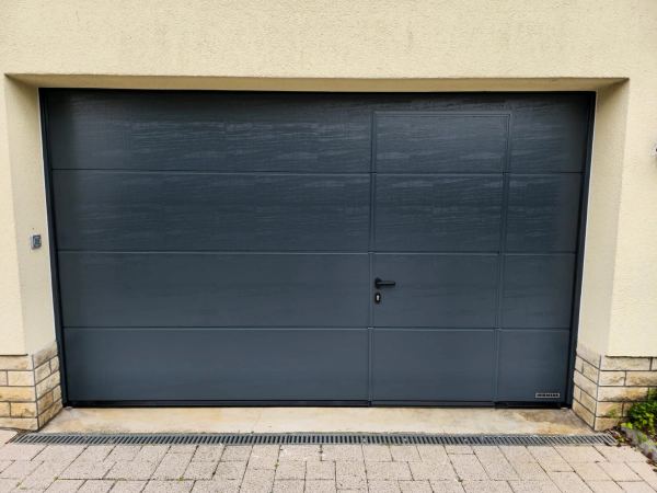Anthrazitgraues Doppel-Sektionaltor in Holzstruktur mit integrierter Schlupftür und schwarzem Griff