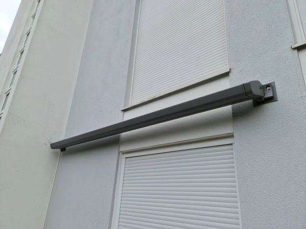 Kompakte graue Markisenkassette geschlossen zwischen zwei Fenstern mit Rollläden