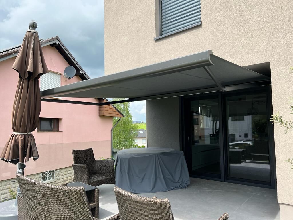 Anthrazit Kassettenmarkise ausgefahren über Terrasse mit Geflechtmöbeln