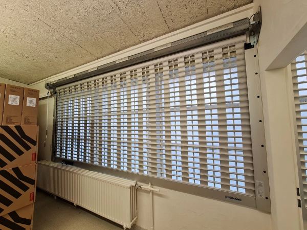 Durchbrochenes Hörmann-Rollgitter innen vor einem großen Fenster montiert