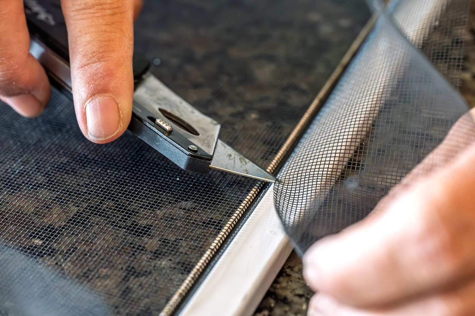 Zuschnitt eines neuen Fliegengittergewebes im Rahmen mit einem Cuttermesser