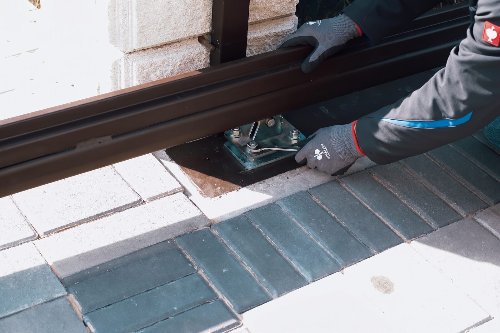 Technician tightening the roller carriage of a sliding gate at the ground rail with a spanner