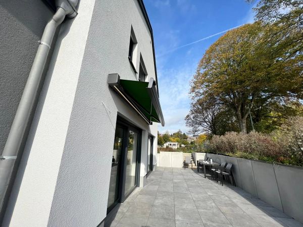 Grüne Markise über einer Schiebetür, lange geflieste Terrasse