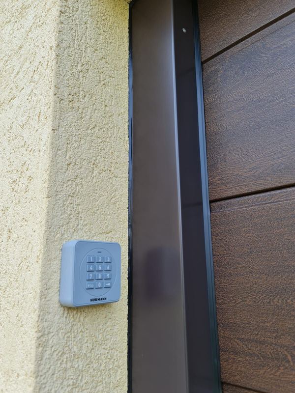 Hörmann-Funkcodetaster an gelber Putzwand neben einem Sektionaltor in dunkler Eichenoptik