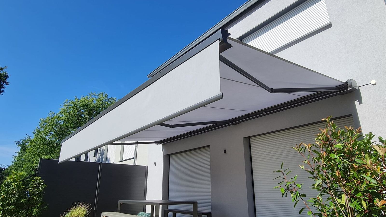 Light grey cassette awning with valance on a modern white house with roller shutters