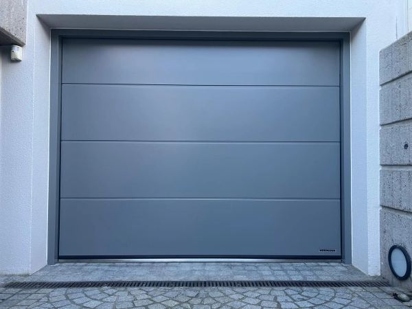 Mittelgraues Hörmann-Sektionaltor mit vier breiten glatten Paneelen, Pflaster mit Rinne