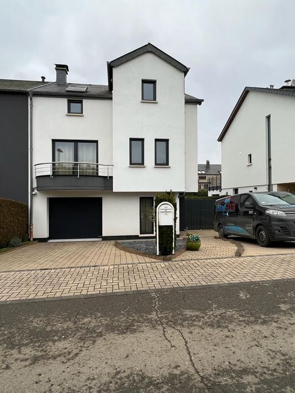Weißes Giebelhaus mit anthrazitfarbenen Fenstern, rundem Balkon und schwarzem Sektionaltor