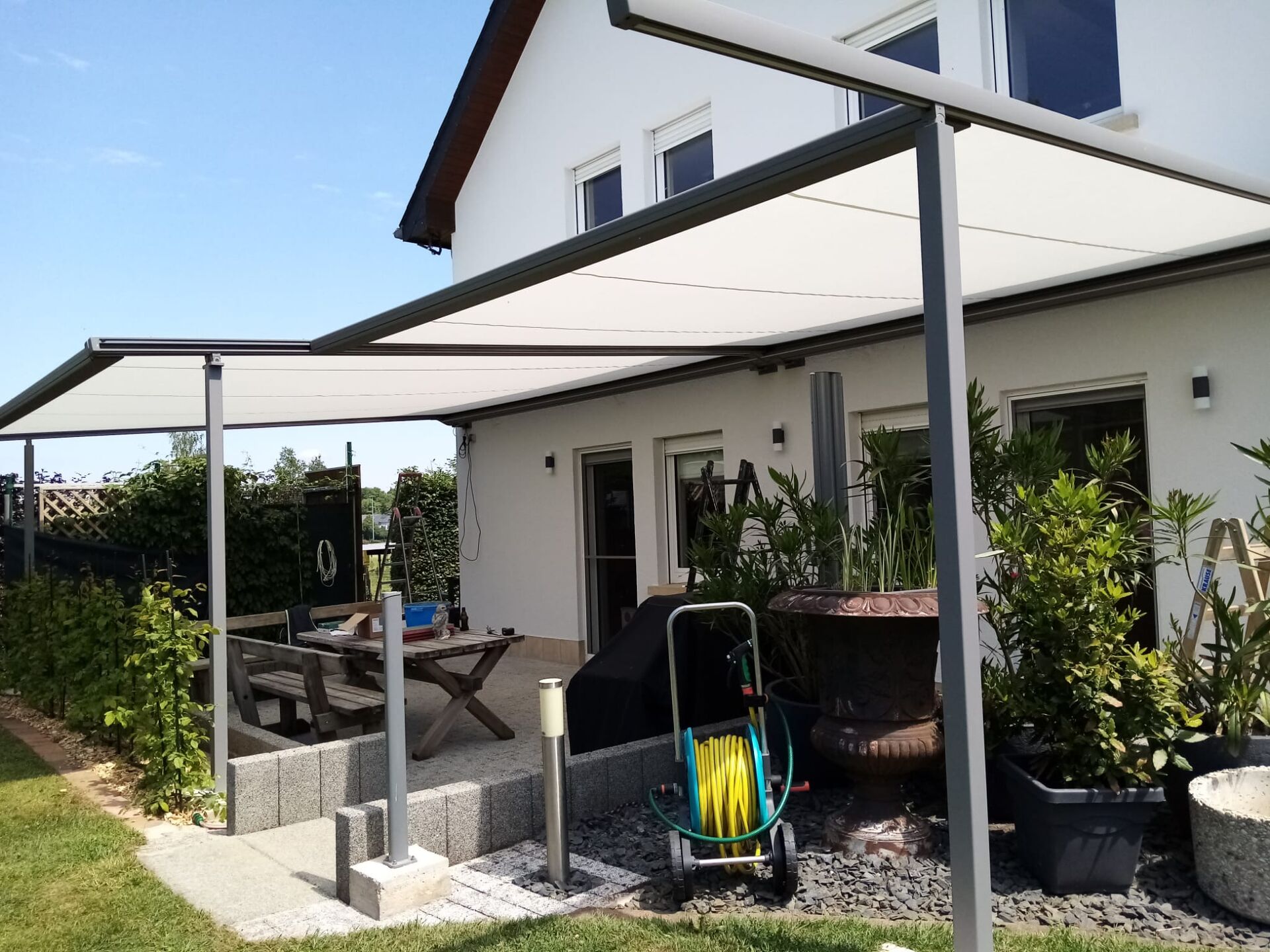 Weiße Pergolamarkise mit zwei Feldern auf Stützen über bepflanzter Terrasse