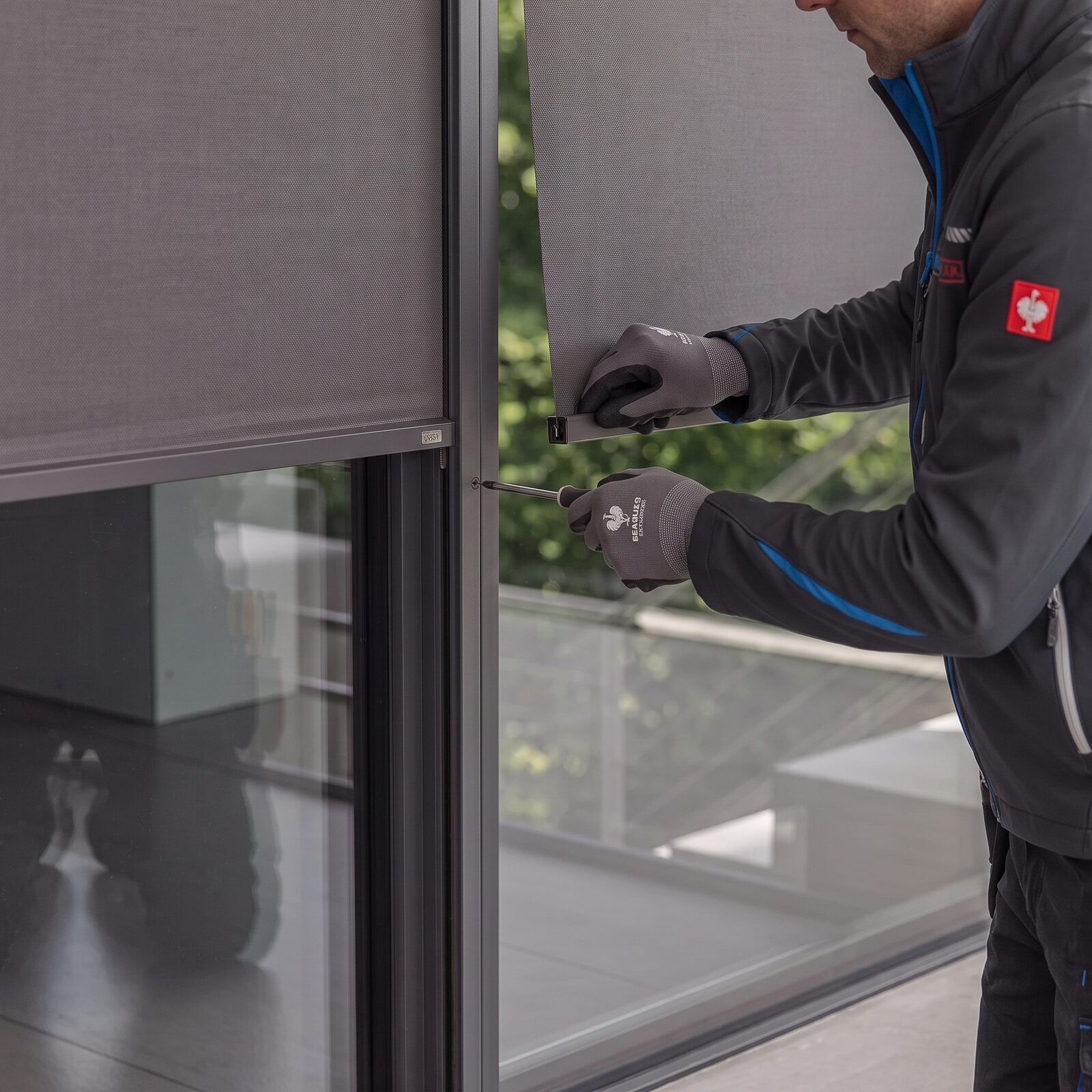 Technician refitting the fabric of a vertical screen into its side channel with a screwdriver