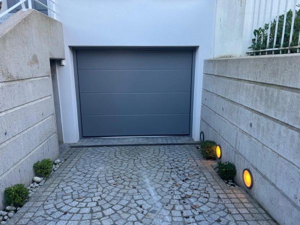 Glattes graues Sektionaltor am Ende einer Rampe mit Bogenpflaster zwischen Betonmauern