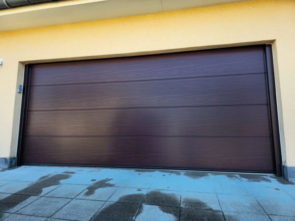 Breites Doppelgaragen-Sektionaltor in dunklem Holzdekor an gelb verputzter Fassade