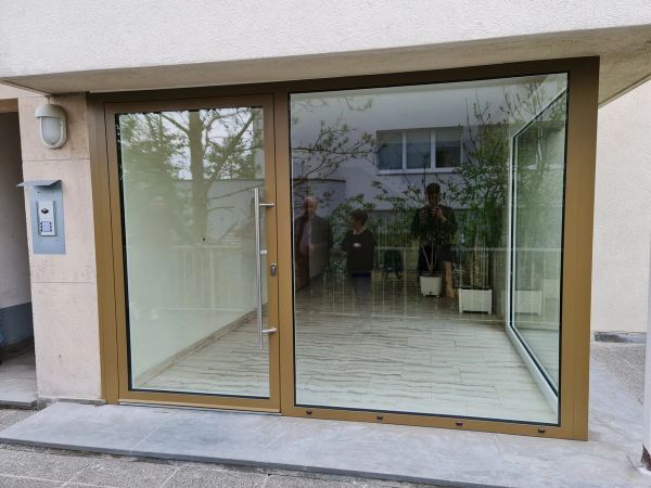 Vollverglaste Hauseingangstür aus goldfarbenem Aluminium mit großem Festfeld und Edelstahlgriff
