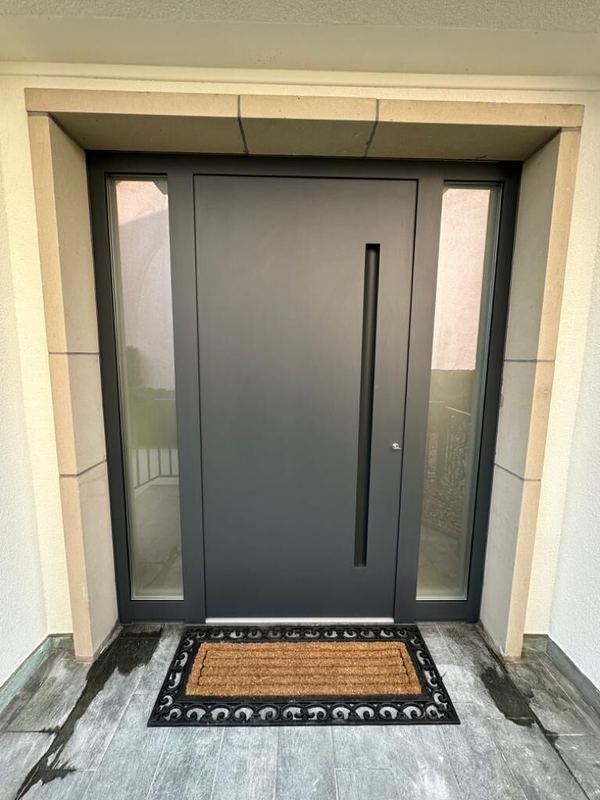 Anthrazit Haustür mit schwarzer Griffmulde zwischen zwei verglasten Seitenteilen, Natursteingewände