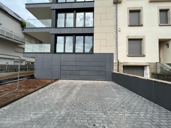 Flächenbündiges Garagentor mit anthrazitfarbener Plattenverkleidung in der Fassade eines Neubau-Wohnhauses