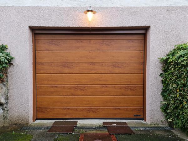 Sektionaltor in Golden Oak unter einer Wandleuchte, hellrosa Putzfassade mit Efeu