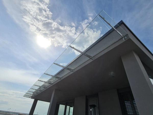 Vordach aus Klarglas auf Edelstahlkonsolen über der Terrasse eines modernen Gebäudes, Untersicht
