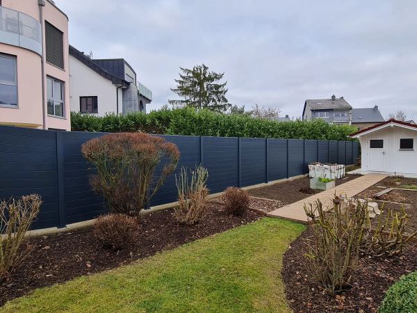 Blickdichter anthrazitfarbener Zaun mit waagerechten Lamellen am Gartenende vor einer Lorbeerhecke