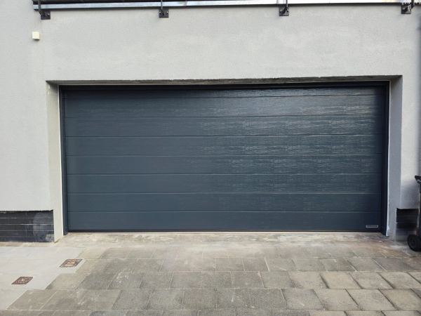 Breites anthrazitfarbenes Sektionaltor mit Holzstruktur in grauer Putzfassade