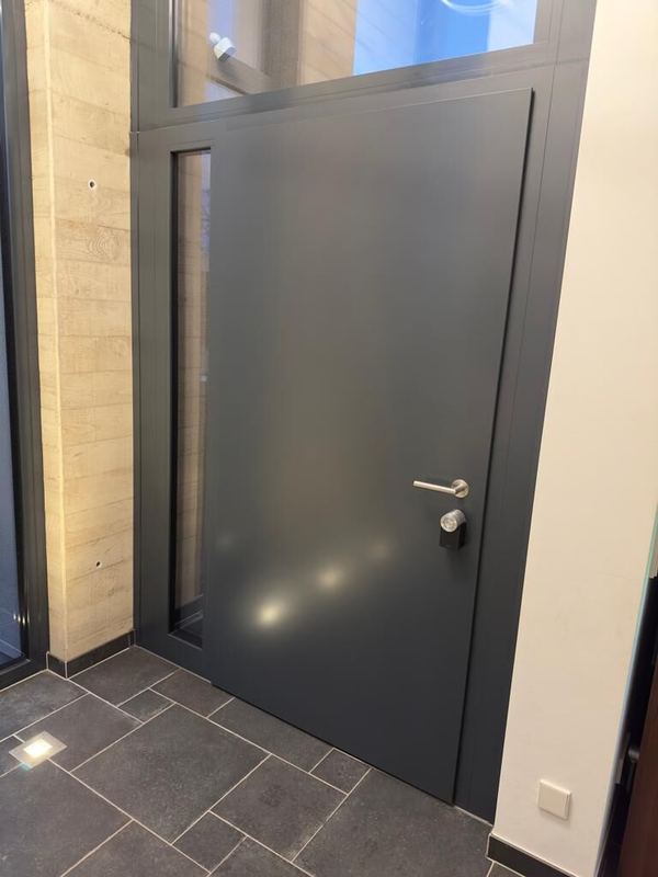 Glatte anthrazitfarbene Haustür mit seitlichem Glasstreifen, Oberlicht und Smart Lock neben Brettschalungsbeton