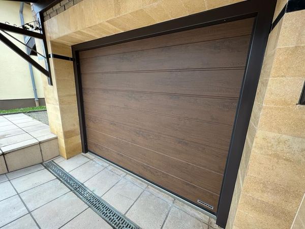Hörmann-Sektionaltor in Nussbaumoptik mit braunem Rahmen, beige Natursteinverkleidung