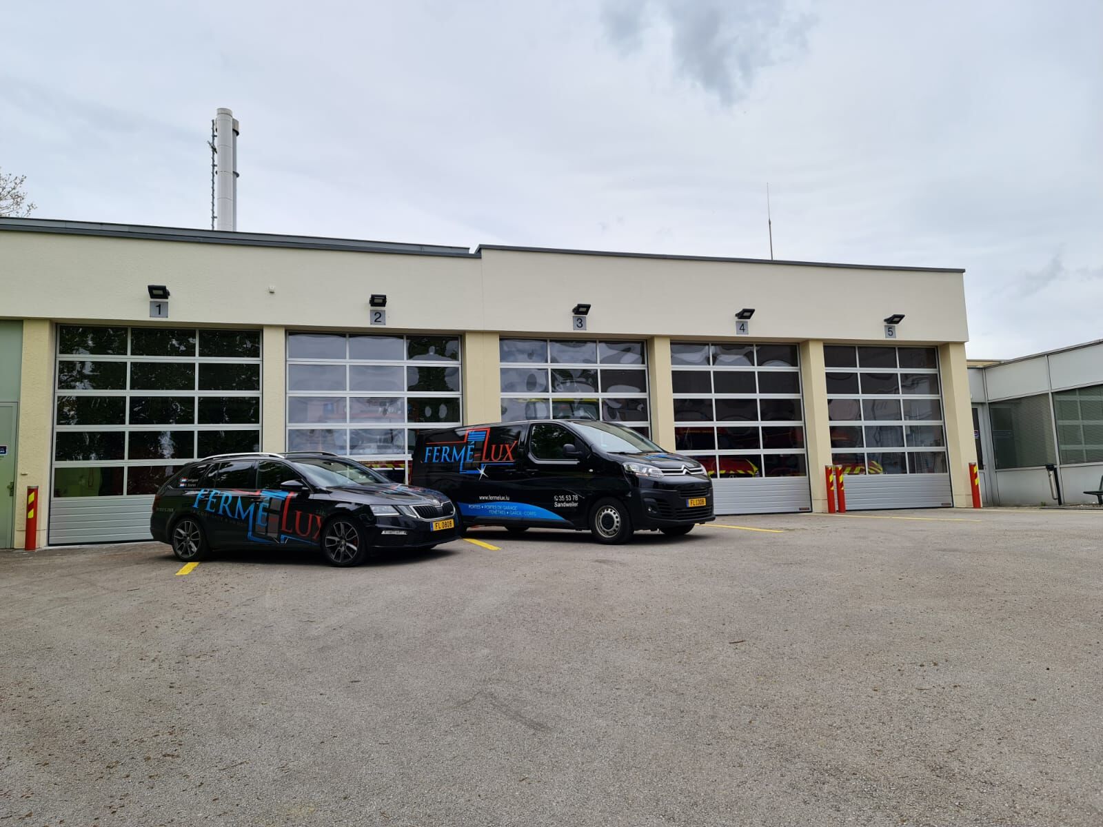 Feuerwache mit fünf verglasten Sektionaltoren und zwei davor geparkten Firmenfahrzeugen